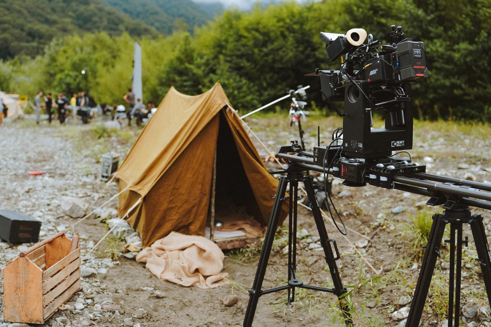 Home Outdoor film scene with professional camera, tent, and crew in forest setting.